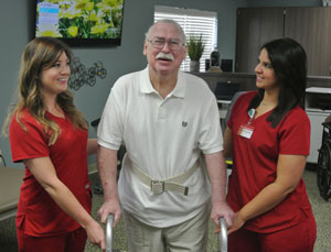 two therapists standing with elderly man using a walker